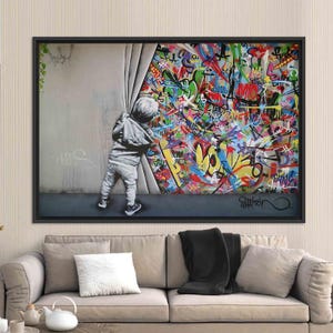 Op de afbeelding: Een kind trekt een gordijn open en onthult een muur bedekt met kleurrijke graffiti. De graffiti bevat het woord "LOVE" en de handtekening van de kunstenaar "Mr. Brainwash".
