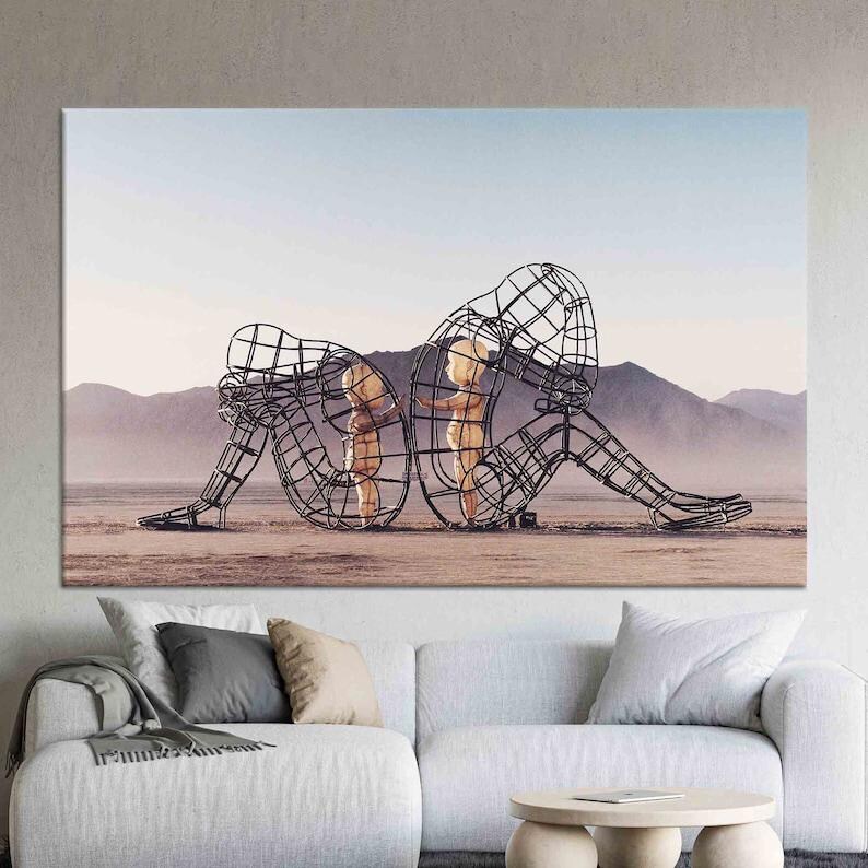 May include: A black metal sculpture of two figures, one larger than the other, standing in a desert landscape. The figures are made of wire mesh and appear to be embracing.