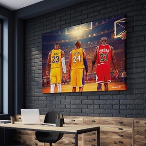 May include: A framed canvas print featuring three basketball players in their jerseys. LeBron James in a yellow jersey with the number 23, Kobe Bryant in a yellow jersey with the number 24, and Michael Jordan in a red jersey with the number 23.