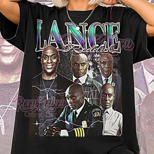May include: Black unisex t-shirt featuring a graphic of Lance Reddick with the text "LANCE Reddick" in a stylized font. The shirt has a crew neck and short sleeves. The words "Unisex Shirt" are printed at the bottom.
