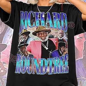 May include: Black unisex shirt featuring a graphic of Richard Roundtree with the text "RICHARD ROUNDTREE" in blue and "Unisex Shirt" in pink. The design includes images of Richard Roundtree in various poses.