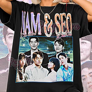 May include: Black unisex t-shirt featuring a graphic of a group of people with the text "NAM & SEO" in purple and orange. The shirt also has the text "Do-san" and "Dal-mi". The words "Unisex Shirt" are at the bottom.