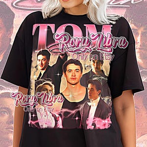 May include: Black unisex shirt featuring a pink graphic with the text "TOM Rory Libra Only on Etsy." The design includes images of men and lightning bolts. The words "Unisex Shirt" are at the bottom.