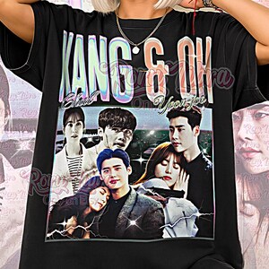 Może przedstawiać: Czarna koszulka unisex z graficznym wzorem z napisem "KANG & OK" i wizerunkami osób. Koszulka ma również napis "Unisex Shirt" na dole. Projekt jest w odcieniach czerni, bieli i szarości.