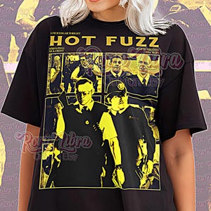May include: Black unisex t-shirt featuring a yellow and black graphic from the movie "Hot Fuzz." The design includes images of the cast and the film's title. The shirt has short sleeves and a crew neck.