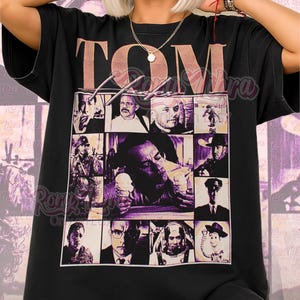 May include: Black unisex t-shirt featuring a collage of images with the word "TOM" in a pinkish-brown font. The shirt has a purple and beige grid design with various images. The text "Unisex Shirt" is at the bottom.