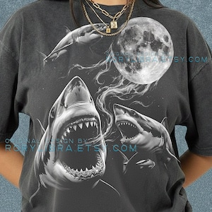 May include: Dark gray t-shirt featuring a detailed graphic of sharks, a full moon, and wispy clouds. The design includes the text "ORIGINAL DESIGN BY RORYLIBRA.ETSY.COM" and "COMFORT COLORS PEPPER".