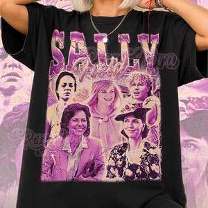 May include: Black unisex t-shirt featuring a collage of images and the name "SALLY FIELD" in a purple, retro-style font. The shirt has the words "Unisex Shirt" in pink script at the bottom.