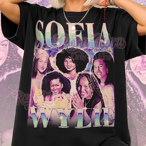 May include: Black t-shirt featuring a graphic of five women with the name "SOFIA WYLD" in a retro style. The shirt has the text "Unisex Shirt" at the bottom. The design is in shades of purple, blue, and yellow.