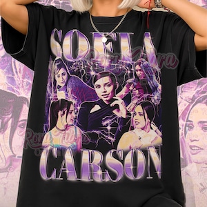 May include: Black unisex t-shirt featuring a graphic of Sofia Carson with a purple and white design. The design includes the name "Sofia Carson" in large, stylized letters, and the text "Unisex Shirt" at the bottom.