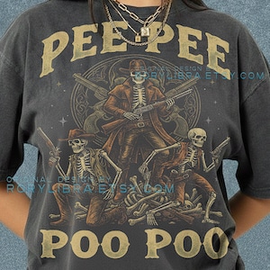 May include: Dark gray t-shirt with a graphic of skeleton cowboys holding guns, with the words "PEE PEE" and "POO POO" in gold lettering. The shirt also has the text "COMFORT COLORS" and "PEPPER".