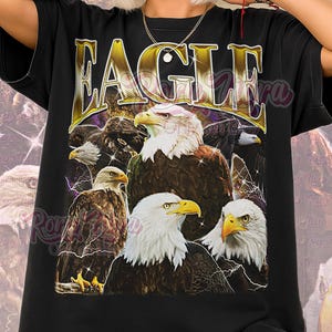 Könnte beinhalten: Schwarzes Unisex-T-Shirt mit einer Grafik von mehreren Adlern. Das Wort "EAGLE" ist in Gold über den Adlern aufgedruckt. Der Text "Unisex Shirt" ist unten in Rosa gedruckt. Die Adler haben weiße Köpfe und braune Körper.