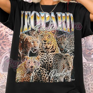 Puede incluir: Camiseta unisex negra con un gráfico de varios leopardos y el texto "LEOPARD Panthera" en un estilo retro. La camiseta también tiene el texto "Panthers" en una fuente de escritura. Las palabras "Unisex Shirt" están en la parte inferior.