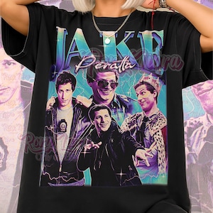 以下が含まれることがあります： 黒色のユニセックスTシャツ。4人の男性のレトロスタイルのグラフィックと、ターコイズと紫色のデザインで「Jake Peralta」というテキストが特徴です。「Unisex Shirt」の文字がピンク色で下部に印刷されています。
