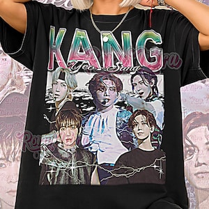 May include: Black unisex shirt featuring a graphic of a musical group with the text "KANG" above the image and "Unisex Shirt" below. The shirt is worn by a person with light skin and blonde hair.