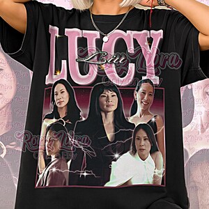 May include: Black unisex t-shirt featuring a graphic of the word "LUCY" in pink, with a picture of several women. The shirt also has the text "Unisex Shirt" in pink. The background is a pink pattern.