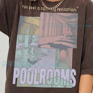May include: A dark brown t-shirt featuring a graphic print of architectural pool room scenes in muted tones. The text "You feel a calming sensation." appears at the top, with the word "POOLROOMS" in large light purple letters below the images.