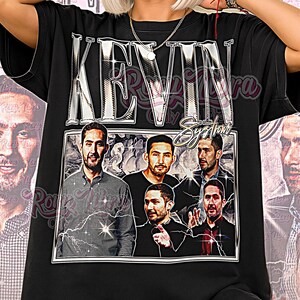 以下が含まれることがあります： 黒色のユニセックスTシャツ。男性グループのグラフィックと、銀色の文字で「KEVIN」と書かれています。Tシャツには「Only on Etsy」と「Unisex Shirt」の文字も入っています。