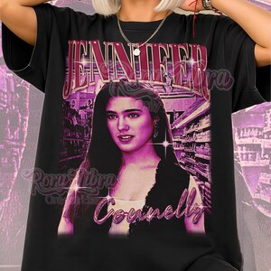 Puede incluir: Camiseta unisex negra con un gráfico morado de Jennifer Connelly, el nombre "Jennifer" arriba y "Connelly" abajo. La camiseta también tiene el texto "Unisex Shirt" en rosa.