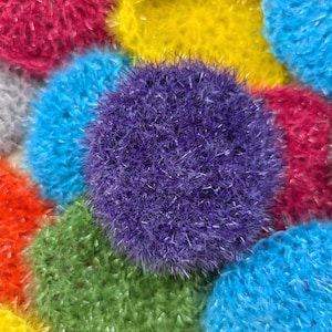 Puede incluir: Primer plano de una colección de artículos redondos de crochet de colores y peludos. Los artículos son de varios tonos de azul, verde, amarillo, rojo y morado.