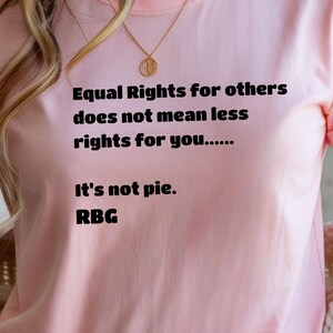 May include: A light pink t-shirt with the text "Equal Rights for others does not mean less rights for you...... It's not pie. RBG" in black. The shirt is worn with a multi-colored sweater.