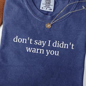 May include: A blue short-sleeved t-shirt with the white text "don't say I didn't warn you" printed on the front. The shirt features a crew neckline and a Comfort Colors brand label on the inside collar, indicating a size small.