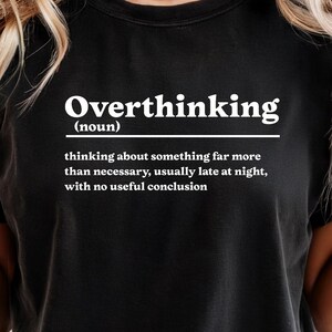 Pode incluir: Camiseta preta com a palavra "Overthinking" em branco, seguida de uma definição. A definição diz: "pensar em algo muito mais do que o necessário, geralmente tarde da noite, sem uma conclusão útil."
