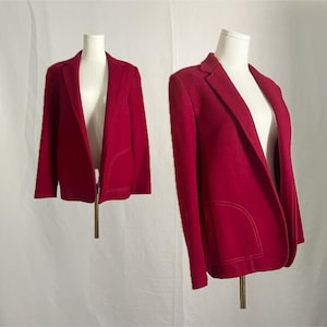 May include: Two red blazers displayed on mannequins. The blazers have a classic design with notched lapels and pockets. The fabric appears to be a soft wool or wool blend. The blazers are displayed against a white backdrop.