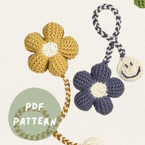 May include: A set of three crocheted flower charms with smiley faces, connected by a braided cord. The flowers are yellow, blue, and white. The text "PDF PATTERN" is on a green circle.