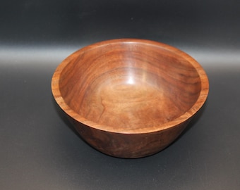 May include: A handcrafted wooden bowl with a smooth, polished finish. The bowl is made of a rich, dark brown wood, showcasing the natural grain patterns. The bowl's interior is a lighter shade of brown.