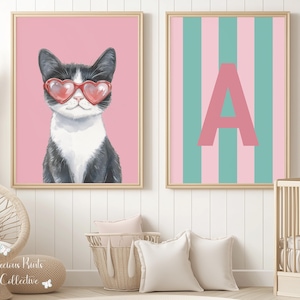 May include: Two framed prints. One features a black and white cat wearing heart-shaped sunglasses against a pink background. The other print has a pink letter "A" on a striped background of pink and teal.