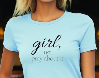 May include: A light blue t-shirt with the text "girl, just pray about it" printed in black.