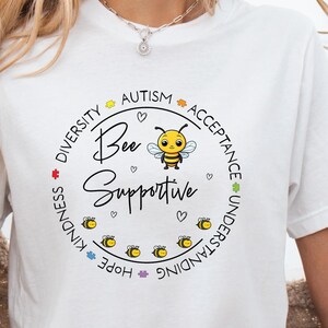 May include: White t-shirt with a graphic of a bee and the text "Bee Supportive" surrounded by a circle of words including "Diversity", "Kindness", "Hope", "Understanding", "Acceptance", "Autism".