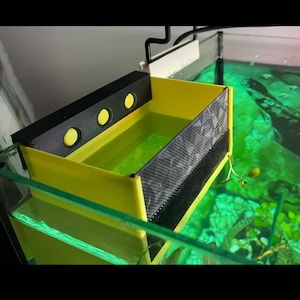 Pode incluir: Um filtro para aquário de plástico amarelo e preto com três luzes amarelas no topo. O filtro está parcialmente submerso em um tanque de água verde.