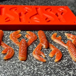 May include: Six red and orange soft plastic crawfish lures, molded in a red silicone mold. The lures are designed to resemble crawfish.