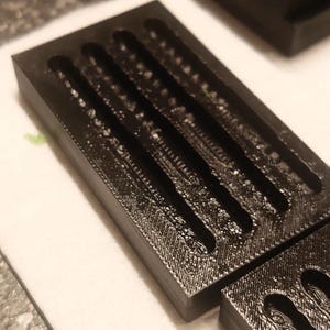 May include: Close-up of several black rectangular moulds with multiple parallel grooves. The moulds appear to be made of a textured material and are arranged on a white surface. The grooves are evenly spaced and run the length of the moulds.