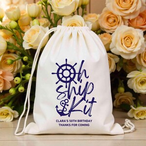 May include: White cotton drawstring bag with a blue nautical design. The bag has a navy blue anchor, a ship's wheel, and the text "Oh Ship Kit" in a navy blue script font. The bag also has the text "Clara's 50th Birthday Thanks for Coming".