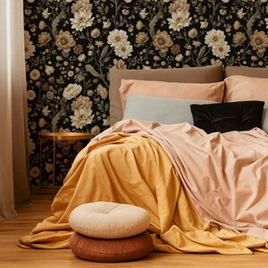 May include: A bedroom scene featuring a bed with peach and mustard-colored bedding, accented by a black pillow. Two round pillows in beige and brown are stacked on the floor. The backdrop is a floral wallpaper with a dark background.