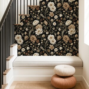May include: A black floral wallpaper featuring cream and brown flowers covers a wall. A built-in bench with a gray cushion sits below the wallpaper. Two round, textured pillows in cream and peach tones are stacked on the floor.