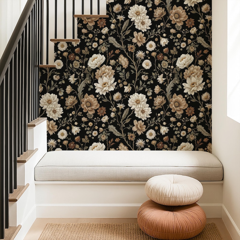 May include: A black floral wallpaper featuring cream and brown flowers covers a wall. A built-in bench with a gray cushion sits below the wallpaper. Two round, textured pillows in cream and peach tones are stacked on the floor.