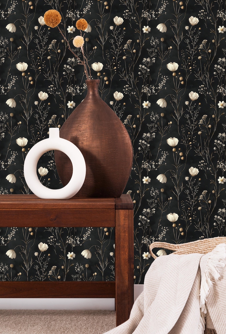 May include: A black and white floral wallpaper with a brown vase and a white ceramic ring holder on a dark wood table. A white blanket is draped over a woven basket.