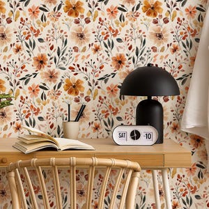 May include: A home office scene featuring a wooden desk with a black lamp, a retro clock, and a potted plant. The background is a floral wallpaper with orange and brown flowers. A white shirt hangs on a wooden ladder.