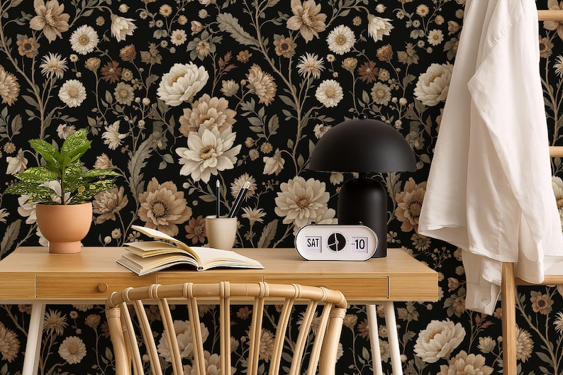 May include: A home office scene featuring a wooden desk with a black lamp, a retro clock, and a potted plant. The background is a floral wallpaper with cream and brown flowers on a black background. A white shirt hangs on a wooden ladder.