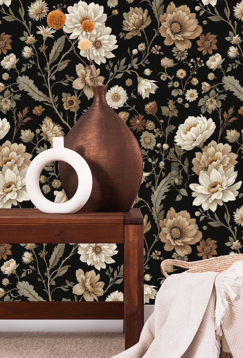 May include: A dark brown wooden table displays a white circular vase and a copper-colored vase against a black floral wallpaper background. The wallpaper features large, cream-colored flowers and smaller brown and tan blooms.