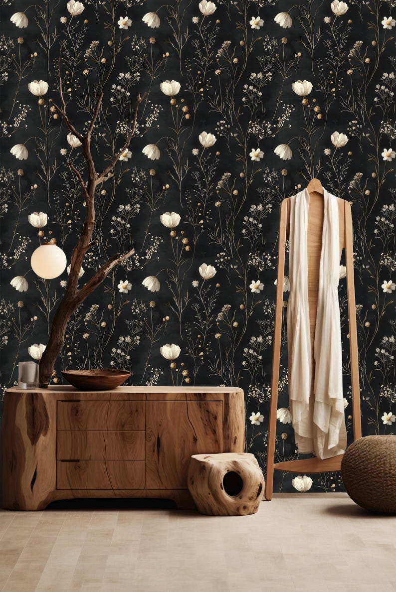 May include: A black and white floral wallpaper with a white flower pattern. The wallpaper is in a room with a wooden dresser, a wooden stool, and a white blanket hanging on a wooden rack.
