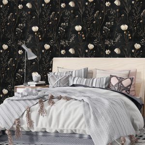 May include: A bedroom with a black and white floral wallpaper featuring white flowers and gold stems. A bed with a white duvet and gray blanket is in the center of the room. Two nightstands with lamps are on either side of the bed.