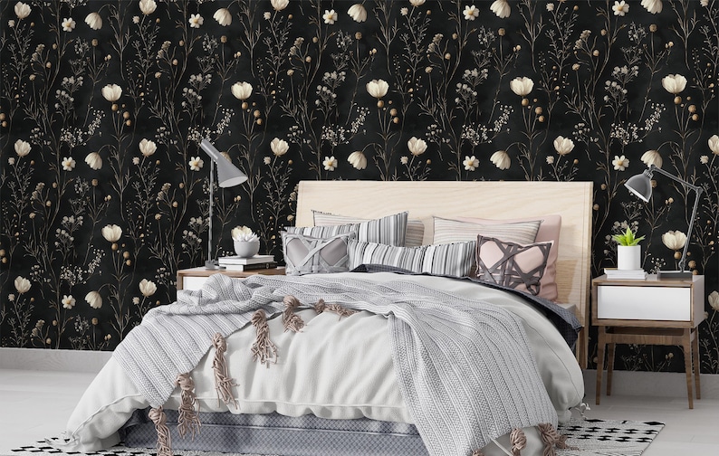 May include: A bedroom with a black and white floral wallpaper featuring white flowers and gold stems. A bed with a white duvet and gray blanket is in the center of the room. Two nightstands with lamps are on either side of the bed.