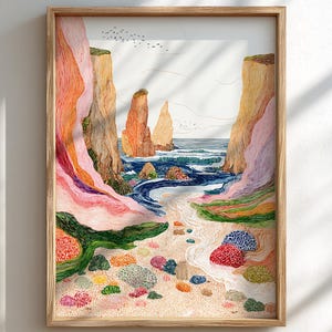 May include: A framed art print depicting a coastal landscape. The artwork features colorful cliffs, a sandy beach, and the ocean. The color palette includes shades of pink, orange, blue, and green. The print is in a natural wood frame.