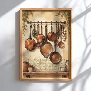 Op de afbeelding: Een ingelijste kunstdruk van een keuken met koperen pannen en keukengerei hangend aan een metalen rek. Daaronder staat een houten plank met keramische potten en een vijzel tegen een achtergrond van tegels met patronen.