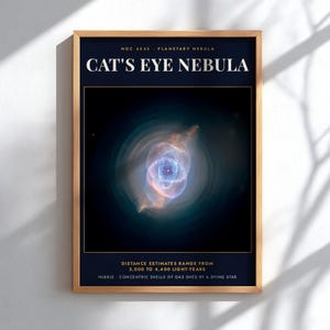 May include: A framed wall print featuring the Cat's Eye Nebula, NGC 6543. The dark blue poster displays the nebula's glowing blue and orange gas shells, with text stating distance estimates of 3,000 to 4,400 light-years and Hubble data.